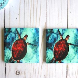 May include: Two square ceramic coasters with a colorful abstract background and a red sea turtle swimming in the water. The turtle has a detailed shell and is swimming in a blue and green watercolor-like background.