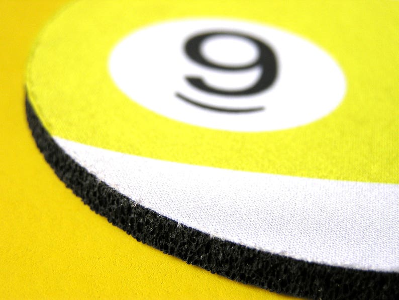 May include: A yellow and white round coaster with a black number 9 in the center. The coaster has a black rubber edge.