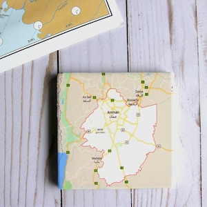 May include: A close-up of a map of Amman, Jordan, showing the city's major roads and landmarks. The map is printed on a light brown background with black lines and text. The city of Amman is highlighted in red.