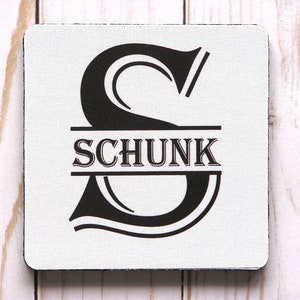 May include: A white square coaster with a black letter "S" and the name "SCHUNK" printed in black.