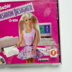 May include: A Barbie Fashion Designer CD-ROM case featuring a blonde doll wearing a light purple sleeveless top and a matching skirt with a heart pattern. The background displays a computer monitor, a printer, and the Mattel Media logo.