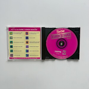 May include: A Barbie Fashion Designer CD-ROM in a clear plastic jewel case. The left insert features a yellow instructional guide titled How To Use Barbie Fashion Designer with icons. The bright pink disc displays the title and Digital Domain logo.