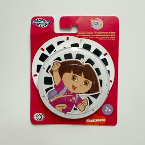 May include: A View-Master reel in its original red cardboard packaging featuring Dora the Explorer. The circular white reel has black image frames and a central graphic of Dora. The packaging includes the text Dora's World Adventure and Nickelodeon.