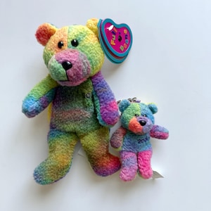 May include: Two plush bears with multi-coloured tie-dye fur in shades of pink, blue, green, and yellow. The larger bear has a heart-shaped tag reading Full Beans and the year 2004 embroidered on its chest. The smaller bear is a keychain.