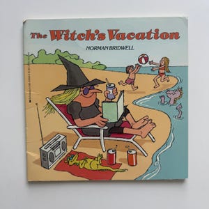 May include: A children's book titled The Witch's Vacation by Norman Bridwell. The cover illustration features a witch in a black hat and dress sitting in a beach chair reading a book, with a radio, drinks, and a green creature on a red towel.
