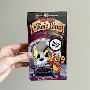 Peut inclure: Une cassette VHS mettant en scène Tom et Jerry dans "Le Magic Ring". La jaquette présente Tom et Jerry dans un décor magique avec un prix de 99 centimes.