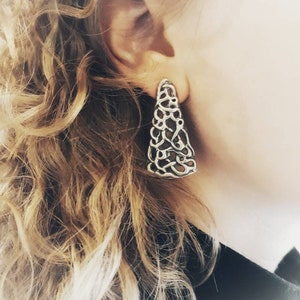 Può includere: Orecchini pendenti in argento con un design delicato e intricato. Gli orecchini hanno la forma di un triangolo e presentano un motivo a filigrana.