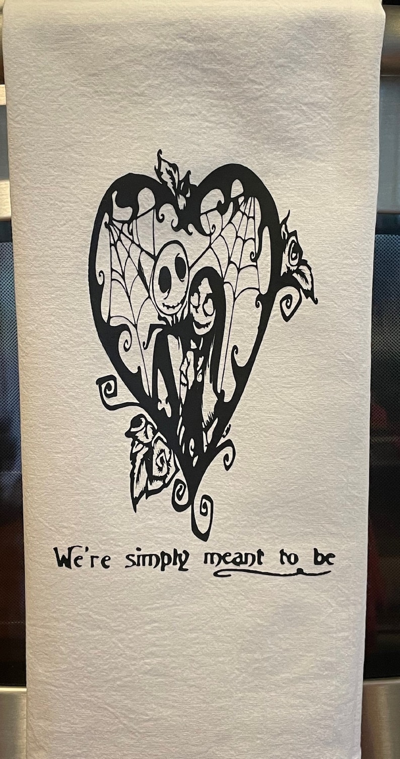 K&ouml;nnte beinhalten: Wei&szlig;es K&uuml;chentuch mit einer schwarzen Grafik von Jack Skellington und Sally aus The Nightmare Before Christmas in einem herzf&ouml;rmigen Design mit Spinnweben und Rosen. Der Text "We're simply meant to be" steht darunter.