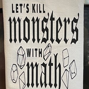 May include: White kitchen towel with black text that reads "LET'S KILL MONSTERS WITH MATH". The towel features illustrations of dice. A fun gift for gamers and math enthusiasts.