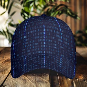 Könnte beinhalten: Dunkelblaue Baseballkappe mit einem Muster aus binärem Code in Hellblau. Die Kappe besteht aus strapazierfähigem Stoff und hat einen gebogenen Schirm. Die Kappe wird auf einer Holzoberfläche mit grünem Laub im Hintergrund gezeigt.