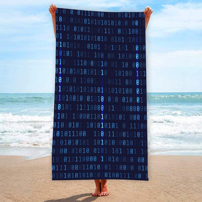 May include: A dark blue beach towel featuring a binary code design in light blue. The towel is held up against a beach backdrop with the sea and sky visible. The binary code is a repeating pattern of 0s and 1s.