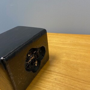 Puede incluir: Caja de madera negra con un recorte en forma de coraz&oacute;n. El recorte est&aacute; lleno de una masa enredada de alambre negro.