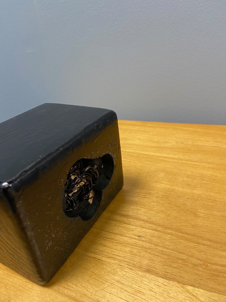 Puede incluir: Caja de madera negra con un recorte en forma de coraz&oacute;n. El recorte est&aacute; lleno de una masa enredada de alambre negro.