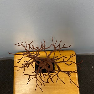 Puede incluir: Una escultura de alambre marr&oacute;n de un &aacute;rbol en una maceta negra, sentada sobre una mesa de madera.