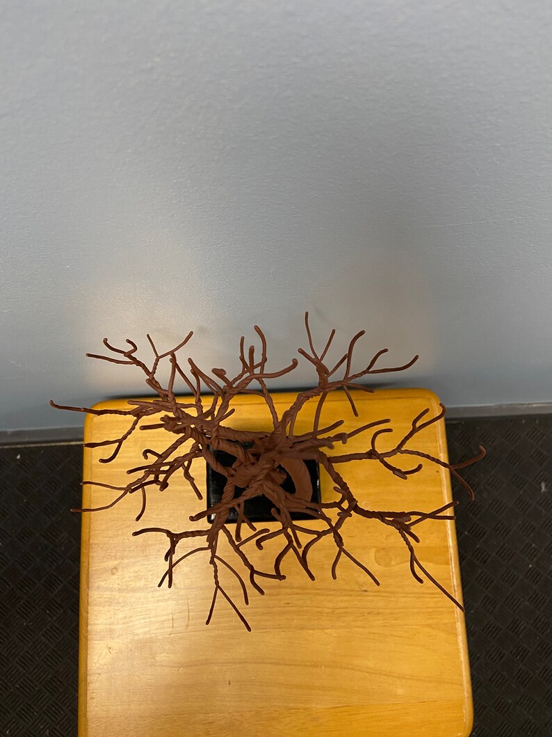 Puede incluir: Una escultura de alambre marr&oacute;n de un &aacute;rbol en una maceta negra, sentada sobre una mesa de madera.