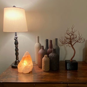 Puede incluir: Una mesa de madera con una l&aacute;mpara, una l&aacute;mpara de sal y una colecci&oacute;n de botellas decorativas. Un peque&ntilde;o &aacute;rbol de ramas secas se encuentra sobre la mesa.