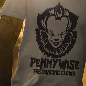 Puede incluir: Una camiseta blanca con una ilustración en blanco y negro de Pennywise el payaso danzante de la película IT. El texto "Pennywise The Dancing Clown" está impreso debajo de la ilustración.