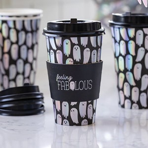 May include: Three black and white disposable coffee cups with a ghost pattern and iridescent accents. The center cup has a black sleeve with the text "feeling FABULOUS".