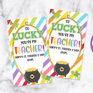 May include: Two printable gift tags with a rainbow striped background and a pot of gold design. The text on the tags reads "So Lucky You're My Teacher! Happy St. Patrick's Day! From."