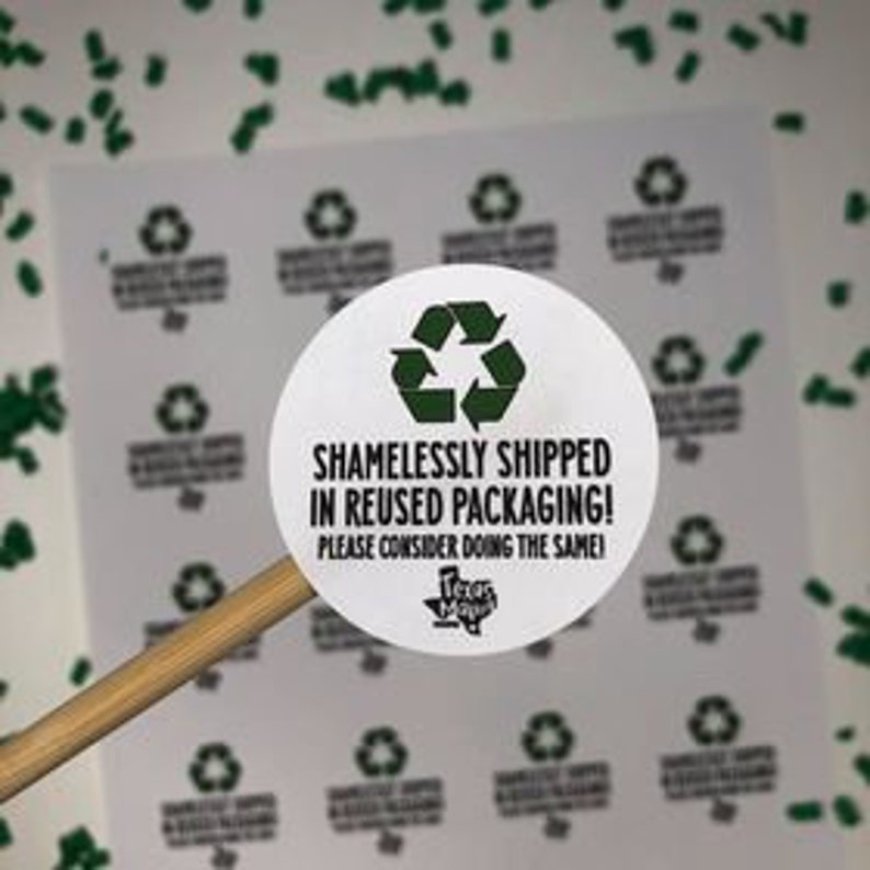 Op de afbeelding: Een ronde witte sticker met een groen recycle-symbool en de tekst "Schaamteloos verzonden in hergebruikte verpakking! Overweeg hetzelfde te doen." De sticker bevat ook het logo "Texas Made".