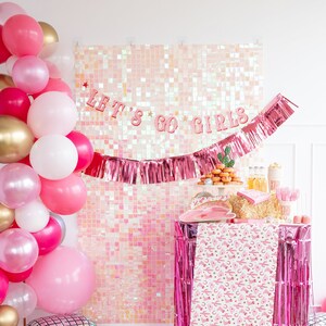 K&ouml;nnte beinhalten: Rosa-goldener Ballonbogen mit einem rosa-wei&szlig;en, schimmernden Hintergrund. Der Hintergrund hat eine rosa Fransen-Girlande und ein rosa Banner mit der Aufschrift "Let's Go Girls".