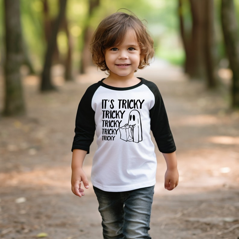 May include: A white and black baseball tee shirt with a ghost holding a trick-or-treat bag. The text on the shirt reads "It's Tricky Tricky Tricky Tricky Tricky".