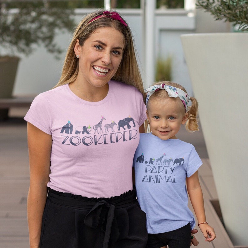 May include: A pink t-shirt with the text "Zookeeper" and a line of animals wearing party hats. A light blue t-shirt with the text "Party Animal" and a line of animals wearing party hats.