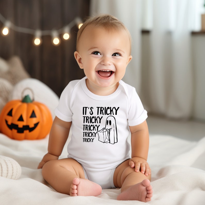 May include: A white baby onesie with a black ghost and the text "It's Tricky Tricky Tricky Tricky Tricky" printed on the front. The baby is wearing the onesie and sitting on a white blanket.