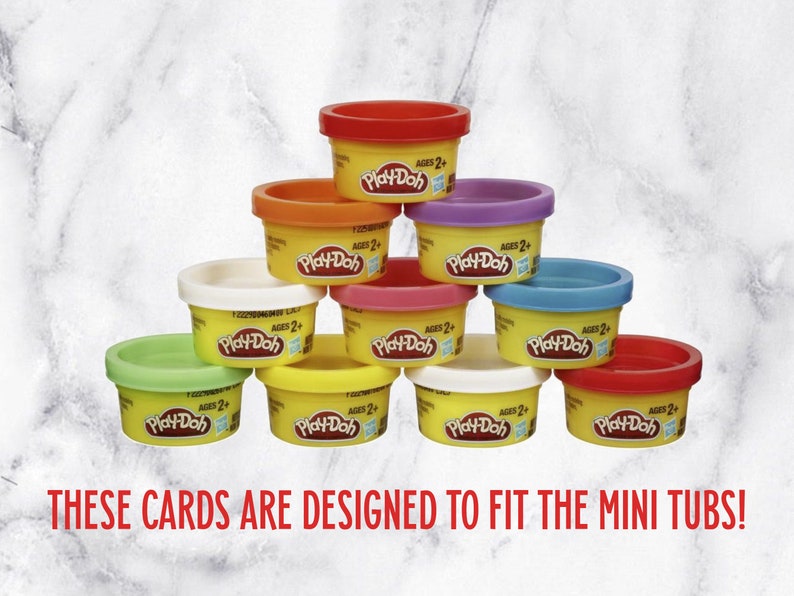 May include: A collection of ten small Play-Doh tubs in various colors, stacked in a pyramid shape. The tubs are yellow with a red, orange, white, green, blue, purple, and pink lid. Each tub has the Play-Doh logo and the text "AGES 2+".
