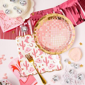 K&ouml;nnte beinhalten: Rosa und goldene Partyteller mit einem Discokugel-Design, rosa und wei&szlig;e Servietten mit einem Kaktus- und Cowboystiefel-Design und silberne Discokugel-Ornamente.