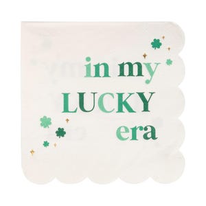 May include: White paper napkins with a scalloped edge. The napkins feature green shamrocks and gold glitter. The text on the napkins reads "I'm in my lucky era".