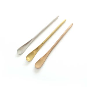 Op de afbeelding: Drie metalen lepels in zilver, goud en roségoud. Elke lepel heeft een lange, slanke steel en een afgeronde, ovaalvormige kom. De lepels zijn diagonaal geplaatst tegen een witte achtergrond.