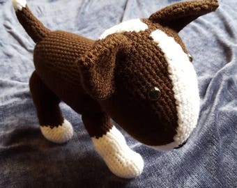 May include: A brown and white crocheted stuffed dog toy. The dog is standing on a blue fabric surface.