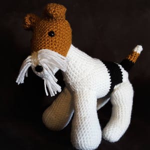 May include: A crocheted stuffed toy dog with white fur, brown ears, and black markings. The dog has a white beard and a black nose.