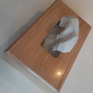May include: A wooden tissue box holder with a rectangular opening for tissues. The box is made of light brown wood with a natural wood grain.