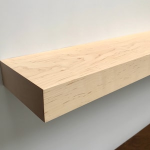 May include: A light wood floating shelf with a natural finish. The shelf is made of solid wood and has a simple, modern design.