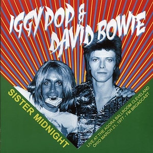 Peut inclure: Une affiche de concert mettant en scène Iggy Pop et David Bowie en noir et blanc. L'affiche a un fond rayé rouge, jaune et bleu avec le texte "Iggy Pop & David Bowie" en grandes lettres blanches. Le texte "Sister Midnight" est en lettres blanches sur un fond vert dans le coin inférieur gauche. Le texte "Live at the Agora Ballroom Cleveland Ohio March 21, 1977 - FM Broadcast" est en lettres blanches sur un fond vert dans le coin inférieur droit.