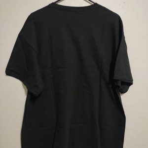 May include: A black t-shirt hanging on a hanger. The t-shirt has short sleeves and a crew neck.