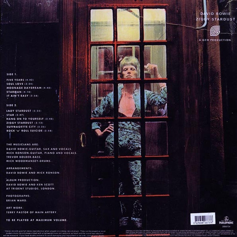 Puede incluir: Una portada de &aacute;lbum de vinilo vintage con un hombre de pelo rojo y una camisa roja de pie en una puerta. La portada del &aacute;lbum es para el &aacute;lbum "Ziggy Stardust" de David Bowie. La portada del &aacute;lbum es una portada de &aacute;lbum de rock and roll cl&aacute;sico.