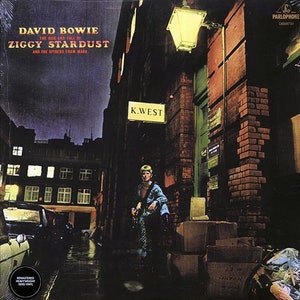 Puede incluir: Una portada de &aacute;lbum de m&uacute;sica con un hombre con un mono azul y blanco estampado de pie en un callej&oacute;n oscuro. La portada del &aacute;lbum es para el &aacute;lbum de David Bowie "The Rise and Fall of Ziggy Stardust and the Spiders from Mars".
