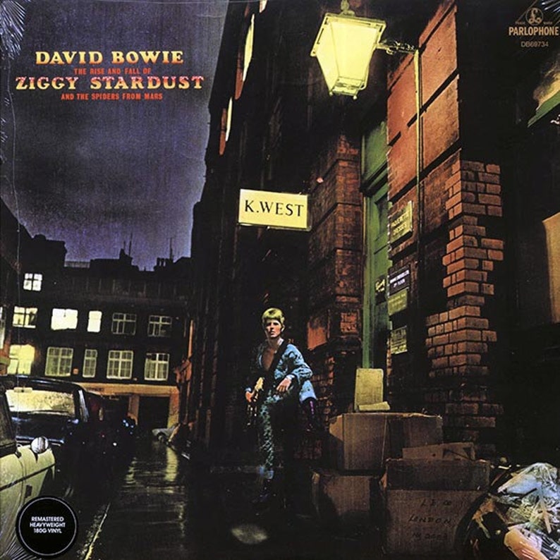 Puede incluir: Una portada de &aacute;lbum de m&uacute;sica con un hombre con un mono azul y blanco estampado de pie en un callej&oacute;n oscuro. La portada del &aacute;lbum es para el &aacute;lbum de David Bowie "The Rise and Fall of Ziggy Stardust and the Spiders from Mars".