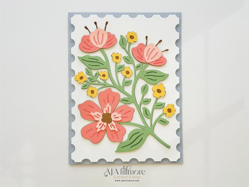 May include: A white card with a blue border and a floral design. The flowers are pink, yellow, and green. The card has the text "AJA fillmore" at the bottom.