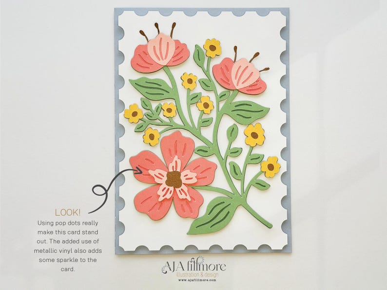 May include: A white card with a scalloped border features a floral design with pink and yellow flowers and green leaves. The text "LOOK! Using pop dots really make this card stand out. The added use of metallic vinyl also adds some sparkle to the card." is printed below the floral design. The text "JA filfmore Illustration & Design www.jafilfmore.com" is printed at the bottom of the card.