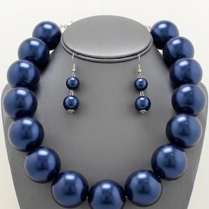 May include: A chunky statement necklace and matching drop earrings set featuring large, round, dark navy blue faux pearls with a smooth, lustrous finish. The necklace consists of a single strand of graduated beads, while the earrings feature two stacked beads.