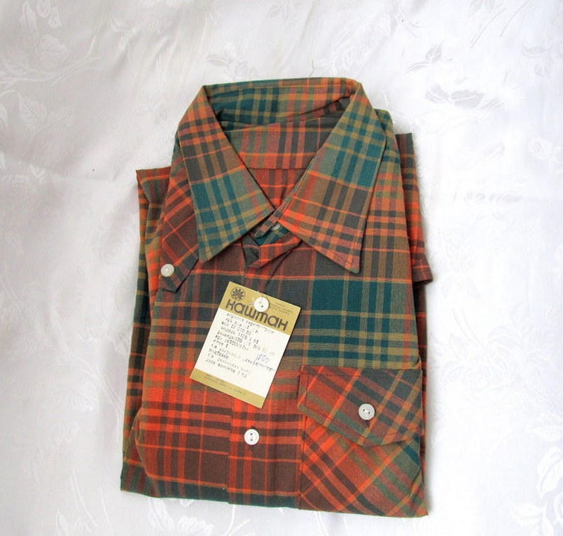 May include: A plaid shirt with a green, orange, and brown color scheme. The shirt has a button-down collar and a pocket on the left side. The shirt has a tag attached that says "Каштан".