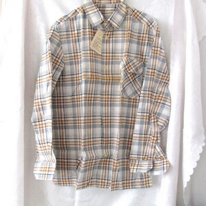 May include: A long-sleeved plaid shirt with a white, brown, and blue plaid pattern. The shirt has a button-down collar and a single chest pocket.
