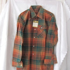 May include: A long-sleeved plaid shirt with a button-down collar. The shirt is orange, green, and brown. The shirt has a pocket on the left side and a tag that says "NOVITCH" on the front.