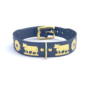 Op de afbeelding: Een marineblauwe hondenriem met goudkleurige metalen accenten. De halsband heeft een gouden gesp en decoratieve gouden koe- en bloemmotieven. De halsband is gemaakt van een flexibel materiaal en is ontworpen om om de nek van een hond te worden gedragen.