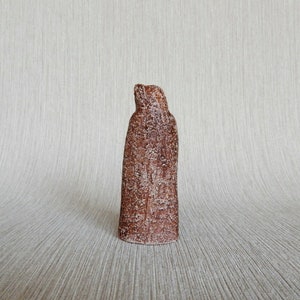 May include: A brown ceramic sculpture of a person wearing a long robe. The sculpture has a rough, textured surface.