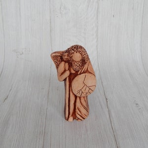 May include: A terracotta figurine of a person holding a shield and a staff. The figurine is brown and has a detailed design.